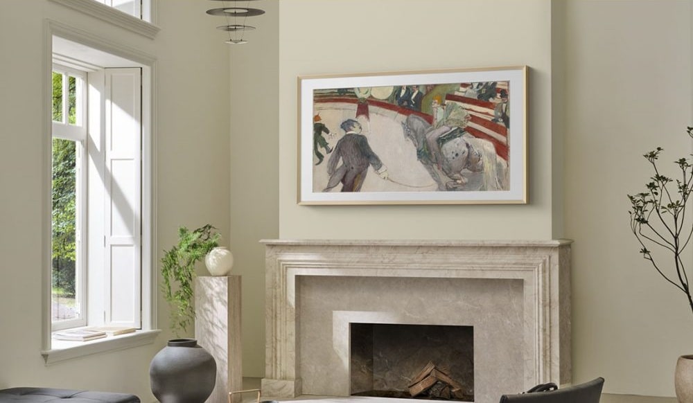 Imagem de uma sala com uma TV Samsung The Frame Pro 4K 2025 montada na parede, exibindo uma obra de arte. A sala apresenta uma decoração moderna, com uma janela aberta, uma lareira de mármore e plantas decorativas.