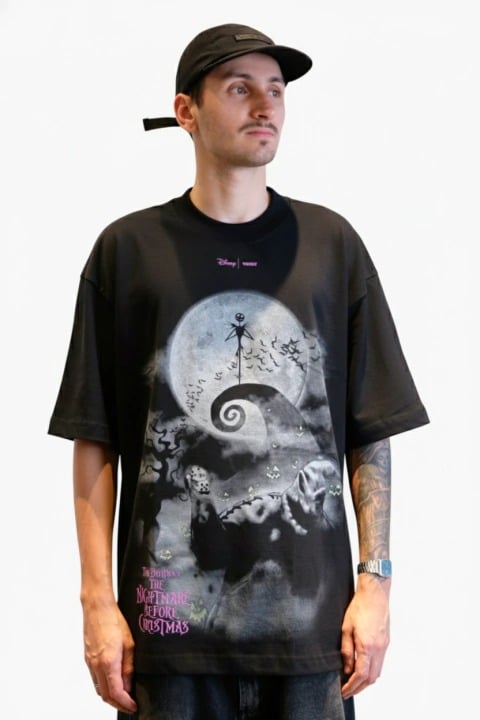 Modelo usando uma camiseta oversized preta com estampa de O Estranho Mundo de Jack, apresentando Jack Skellington no topo de uma colina e uma lua cheia ao fundo.