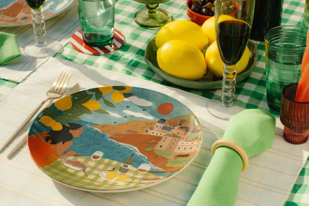 Uma mesa de verão decorada com pratos coloridos, copos, garrafas e limões, destacando uma atmosfera vibrante e alegre.