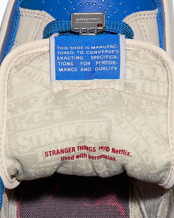 Interior do tênis Converse Weapon, mostrando a etiqueta azul com instruções de fabricação e a inscrição em vermelho 'STRANGER THINGS ™© Netflix'.