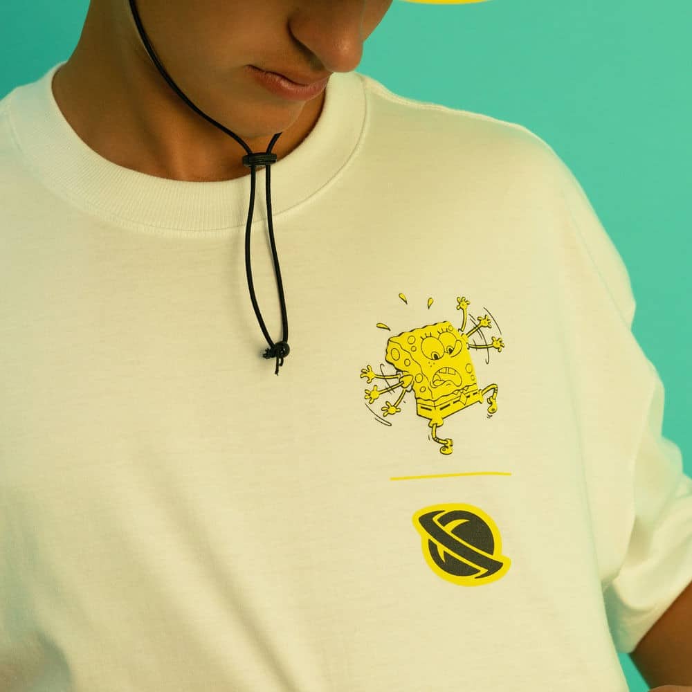 Modelo usando camiseta branca com estampa do Bob Esponja e logotipo da marca Lost, em fundo azul.