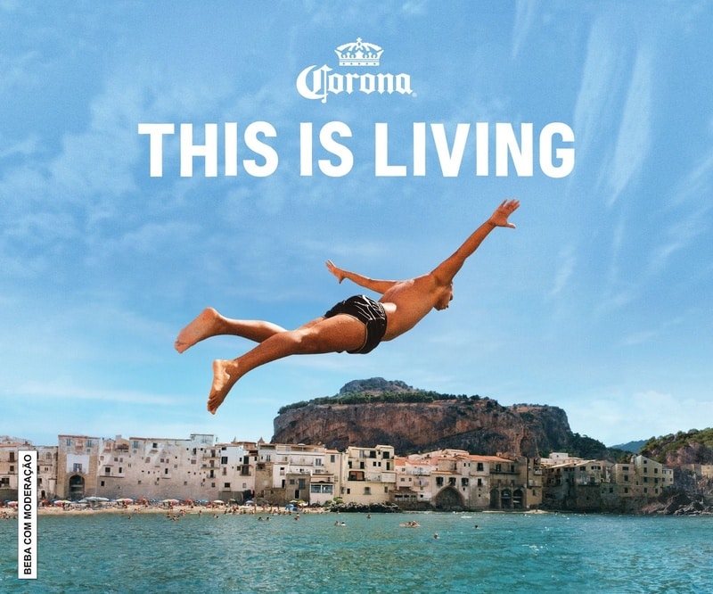 Um rapaz saltando no ar em direção ao mar, com uma cidade costeira ao fundo. O texto 'THIS IS LIVING' está escrito acima da imagem.