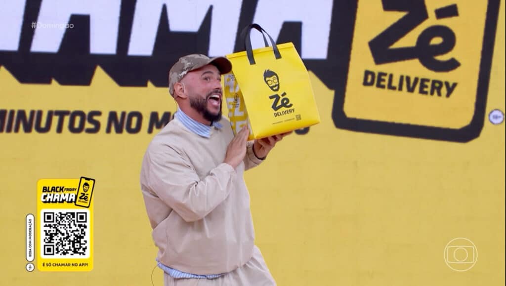 Um apresentador sorridente segurando uma sacola amarela do Zé Delivery em um cenário colorido, promovendo a campanha de Black Friday.