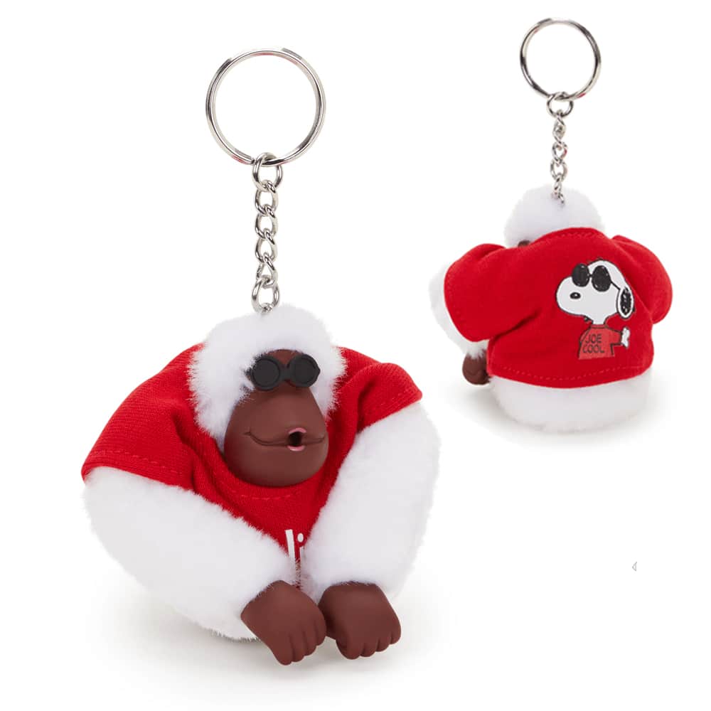 Chaveiro do macaco Joe Cool da Kipling, vestido com uma camiseta vermelha e óculos escuros, com estampa do Snoopy. Apresenta um design divertido e sofisticado, ideal para colecionadores.