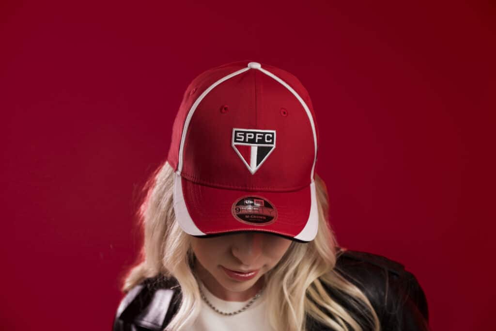 Modelo de boné vermelho da coleção New Era inspirado no São Paulo FC, com logo SPFC na frente e a pessoa usando um olhar voltado para baixo.