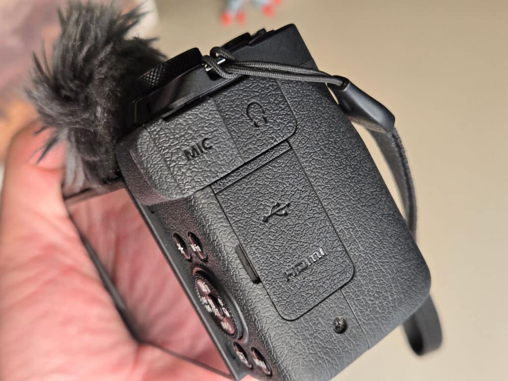 Visão detalhada da parte superior e lateral da câmera Canon PowerShot V1, mostrando conexões de microfone, HDMI e USB, além de um revestimento texturizado para melhor aderência.