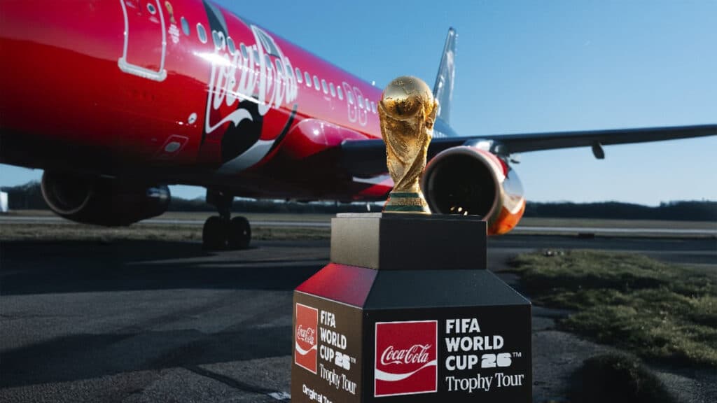 Taça da Copa do Mundo FIFA 2026 em frente a um avião vermelho da Coca-Cola.