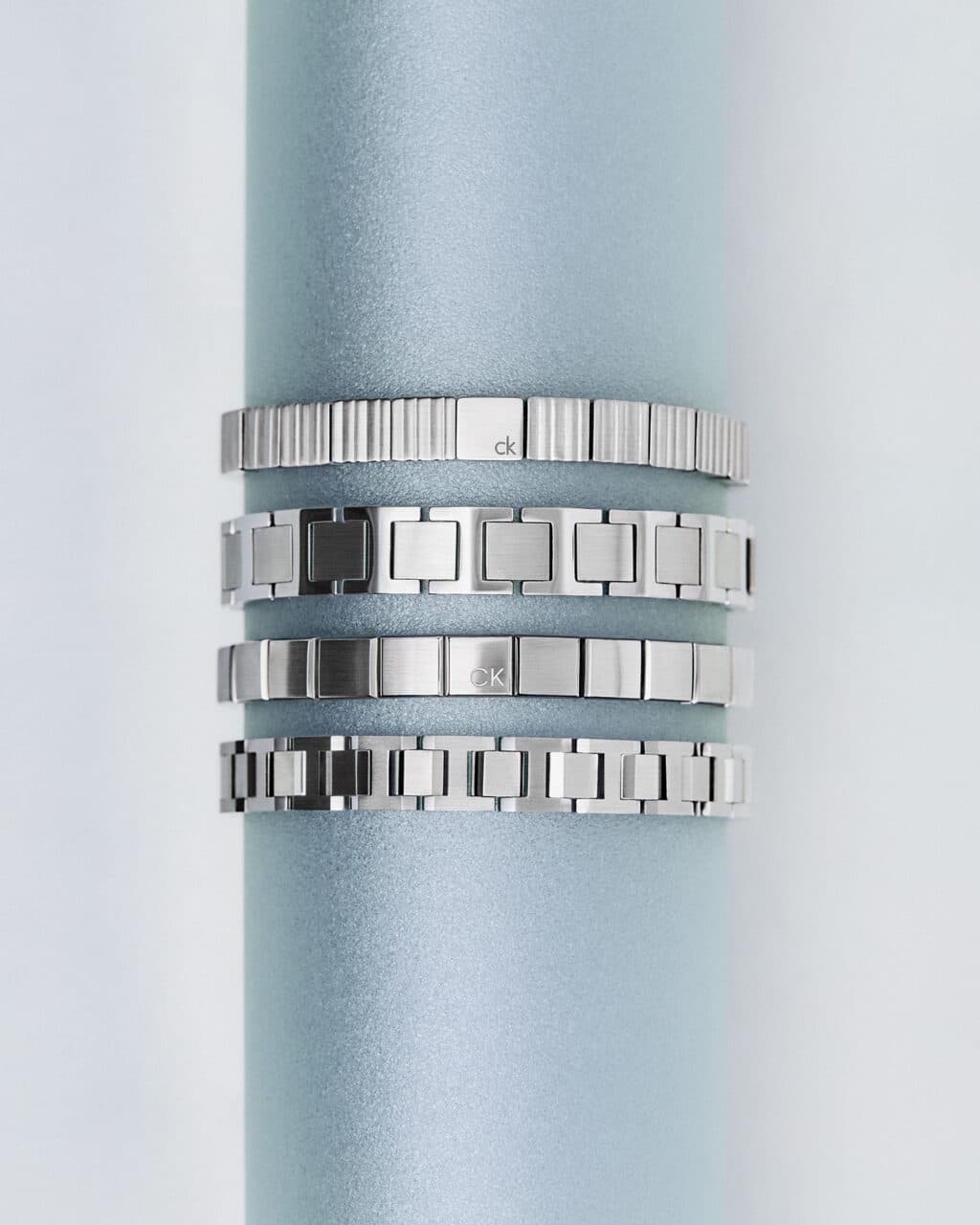 Conjunto de pulseiras de aço inoxidável da Calvin Klein, apresentando diferentes texturas e acabamentos em um fundo suave.