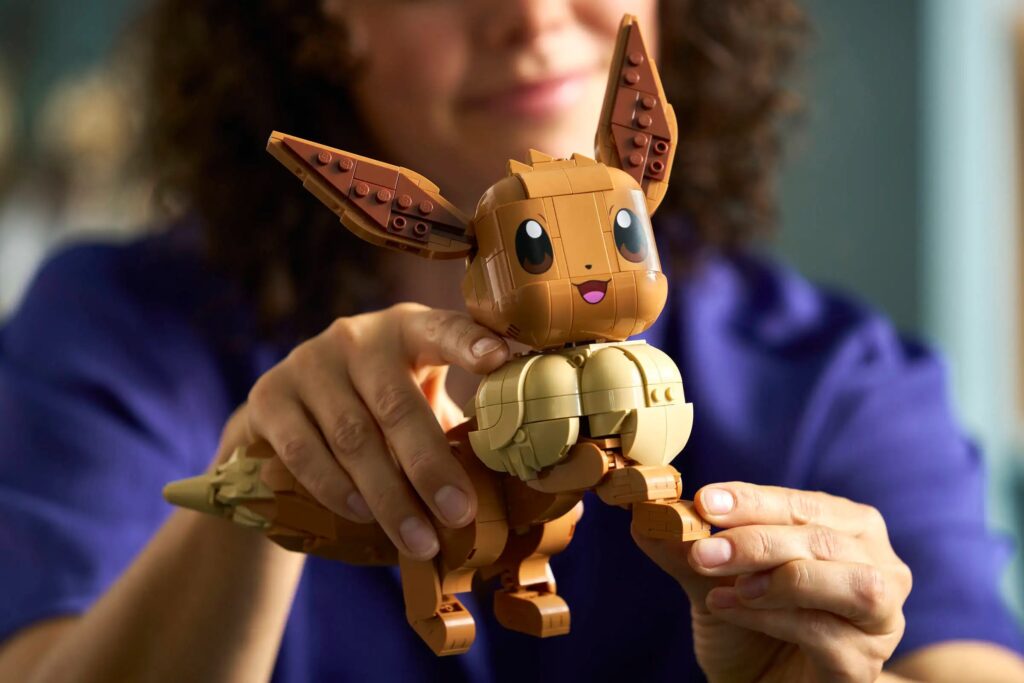 Pessoa segurando uma figura de LEGO do Pokémon Eevee, com detalhes em marrom e bege, enquanto sorri para a câmera.
