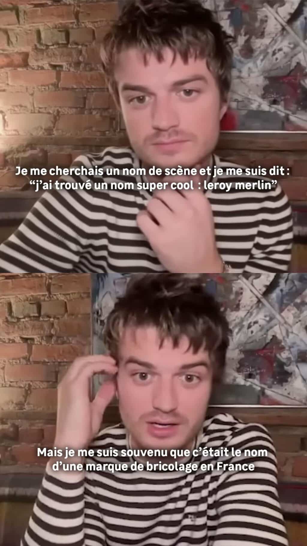 Joe Keery falando em um vídeo, vestindo uma camiseta listrada, com um fundo de tijolos e arte na parede, mencionando em francês a busca por um nome artístico e a descoberta de que 'Leroy Merlin' é o nome de uma marca de bricolagem.