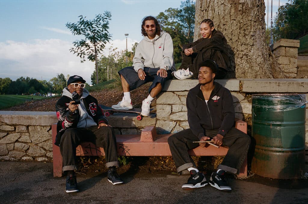 Quatro pessoas sentadas em um banco de pedra em um parque, vestindo peças da coleção Levi's x Jordan. Um deles está segurando uma câmera, enquanto outro segura um par de baquetas.