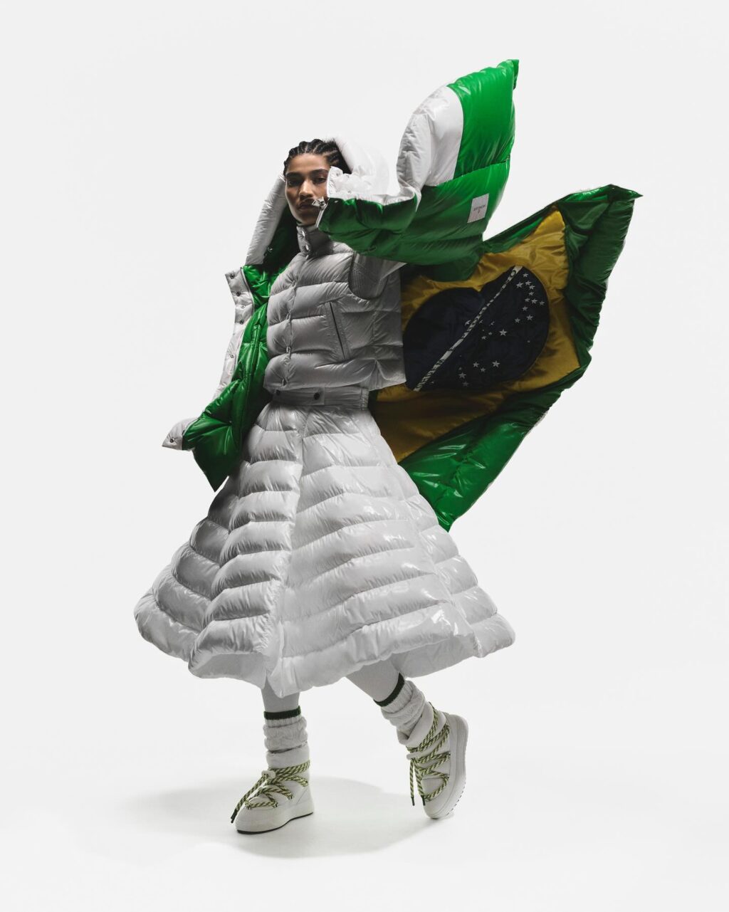 Uma modelo vestindo uma jaqueta puffer oversized exclusiva em verde e prata, combinada com uma saia puffer da mesma cor, exibindo um design de moda criativo contra um fundo branco liso.