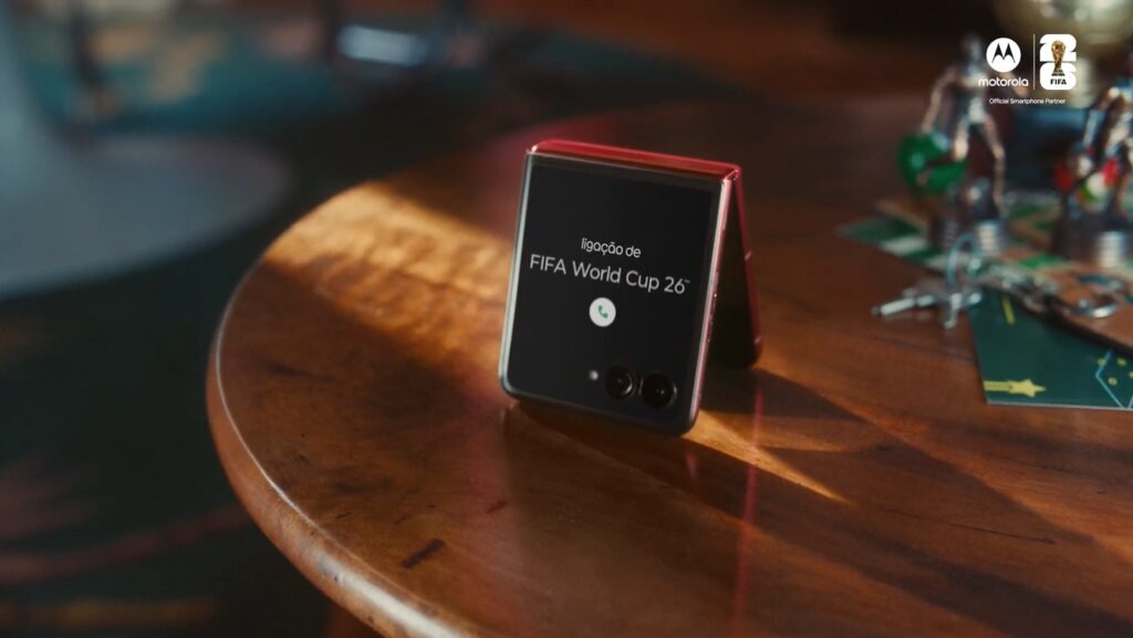 Smartphone da Motorola com logo da FIFA World Cup 2026 exibido em uma mesa de madeira ao lado de objetos de festa.