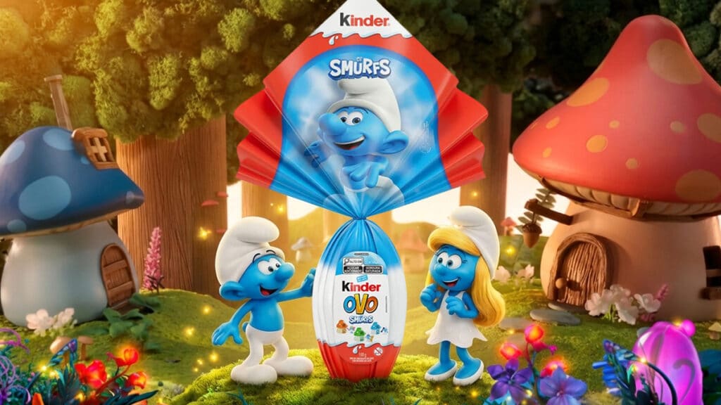 Uma embalagem colorida de chocolate Kinder com os Smurfs, com dois personagens Smurfs ao lado, em um cenário de floresta lúdico com casas de cogumelo.