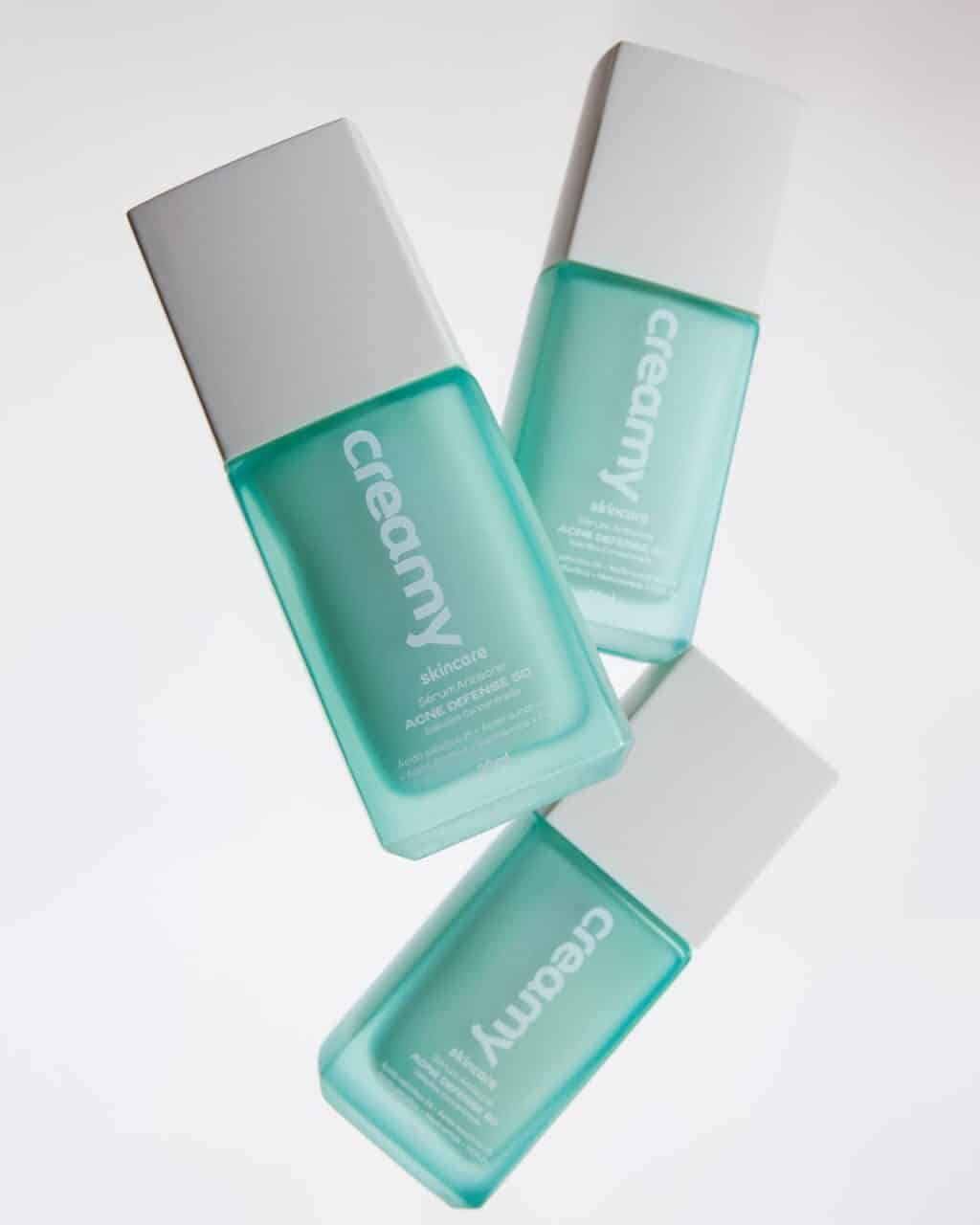 Three teal skincare serum bottles with white caps, labeled 'creamy skincare' and 'ACNE DEFENSE SD', against a light background.