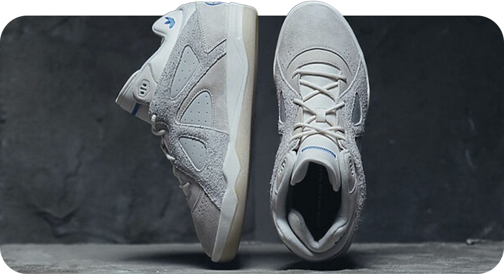 Um par de tênis cinza-claro exibidos de lado e de cima, apresentando uma mistura de camurça e malha, com detalhes em azul.