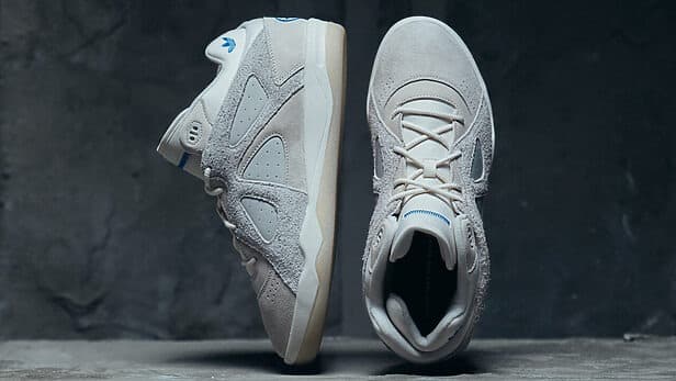 Um par de tênis estilosos em tons de cinza claro e branco, exibidos em ângulos laterais e superiores, apresentando elementos de design exclusivos e materiais texturizados.