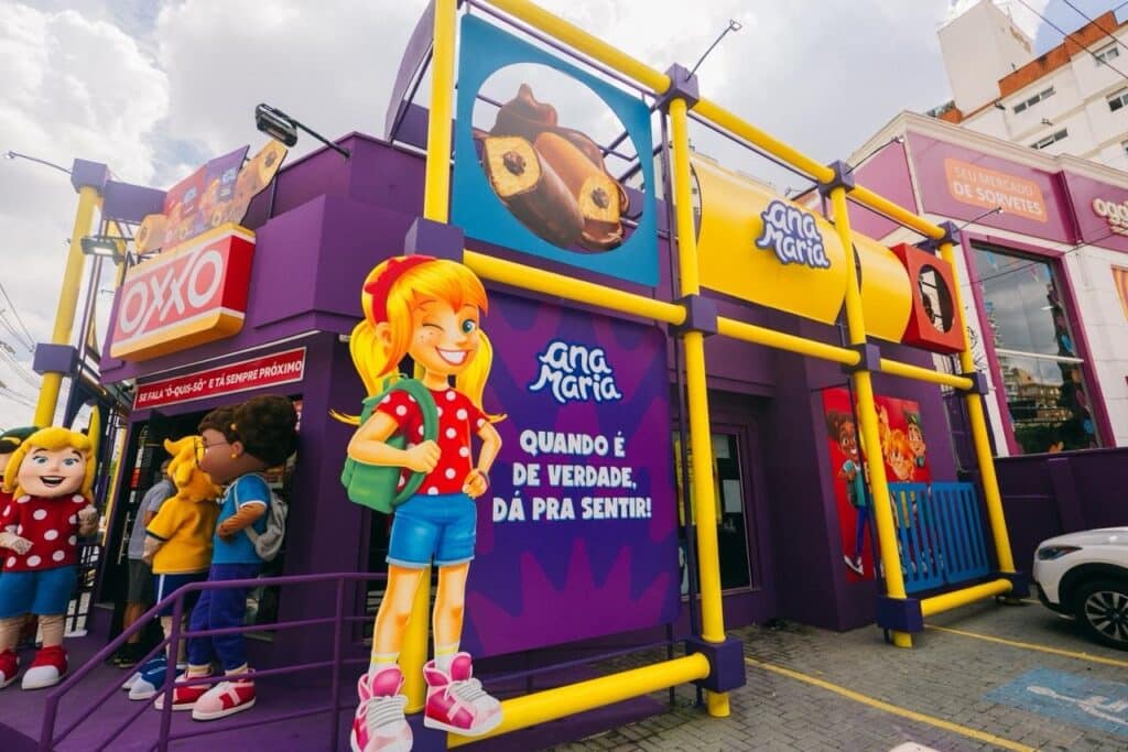 A colorful storefront featuring the OXXO logo and animated characters outside, including a blonde girl with pigtails and a girl in a polka dot dress, representing the Ana Maria brand.