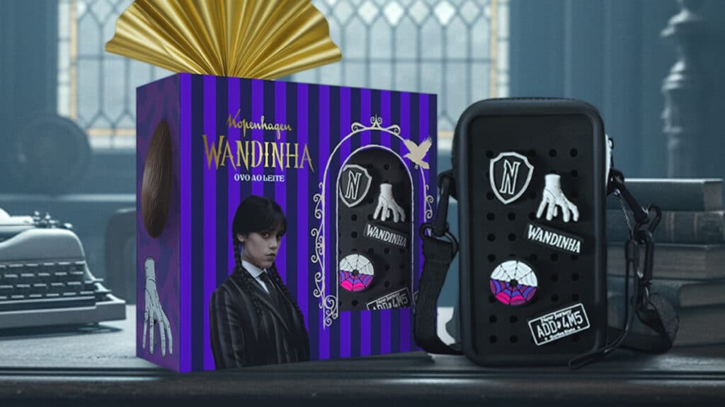 Uma caixa de presente com um design roxo e preto com o nome 'Wandinha' e um laço dourado, acompanhada de uma sacola preta adornada com diversos adesivos temáticos, incluindo um símbolo de mão e uma teia de aranha, sobre um fundo com pouca luz.
