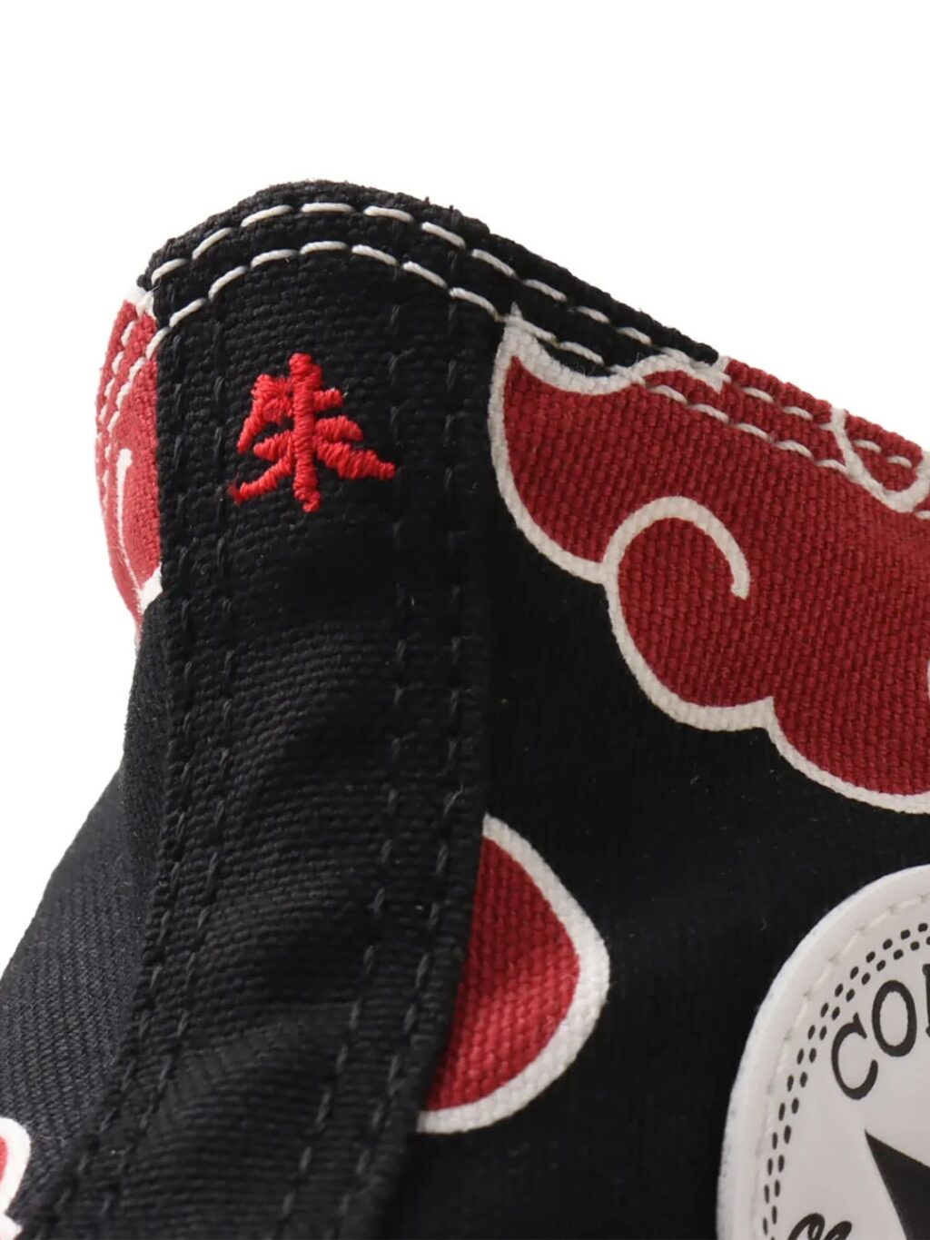 Detalhe de um tecido preto com padrões de nuvens vermelhas e costuras brancas intrincadas.