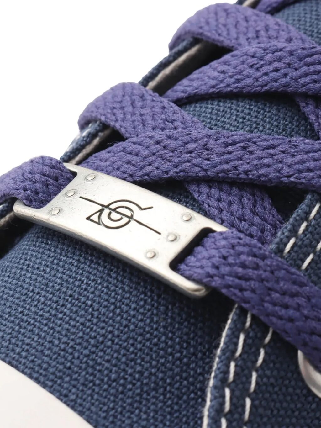Detalhe de um tênis azul com cadarços roxos e um fecho de cadarço metálico com um desenho.