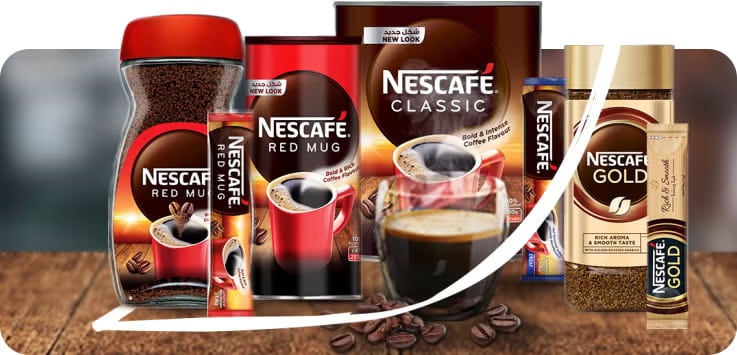 Exposição de produtos de café Nescafé, apresentando as variedades Nescafé Classic, Red Mug e Gold, ao lado de uma xícara de café e grãos de café sobre uma superfície de madeira.