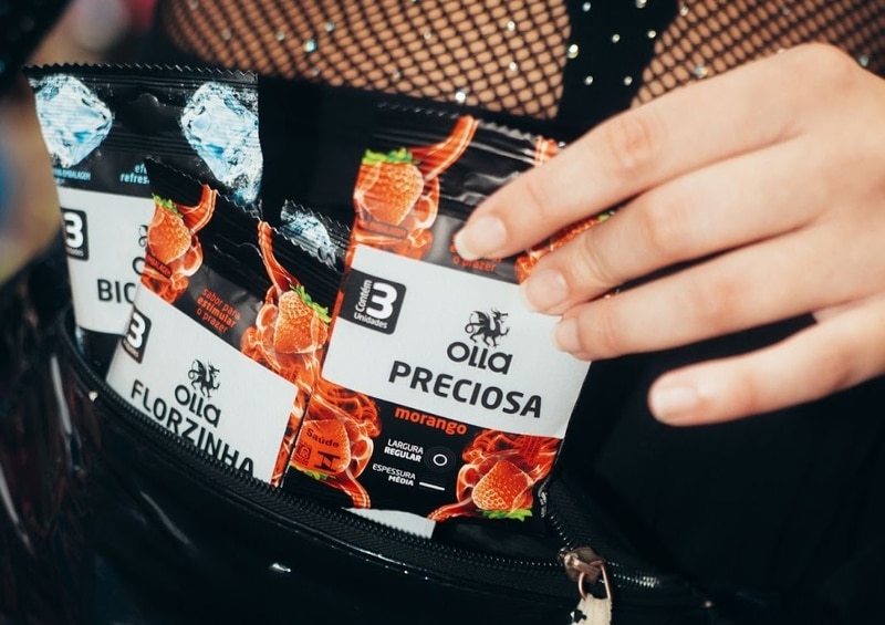 Um close de uma mão alcançando o interior de uma sacola com zíper contendo várias embalagens de produtos Olla, incluindo sabores como 'Preciosa' e 'Florzinha'.