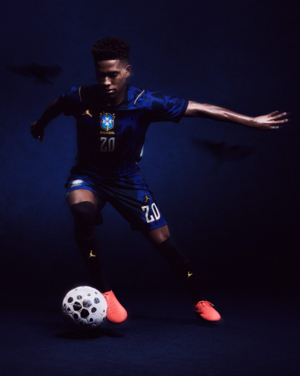 A soccer player in a blue Brazil jersey is skillfully dribbling a white soccer ball, set against a dark background with subtle shadows.