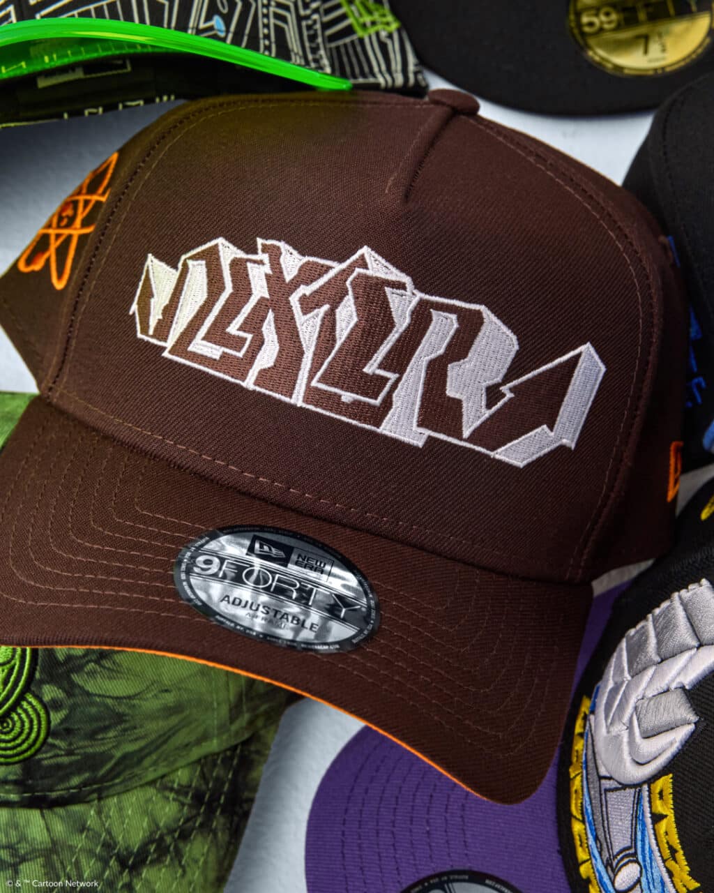 A close-up of a brown cap featuring a stylized white logo on the front, labeled 'Dexter', with other colorful caps in the background.