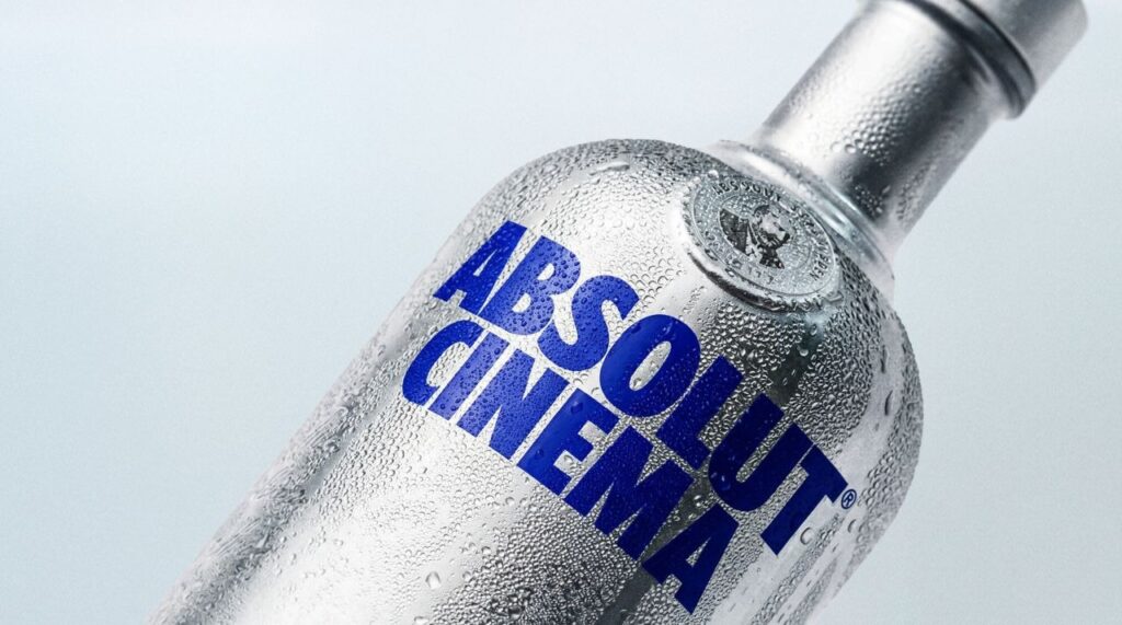 Um close-up de uma garrafa de vidro fosco de vodka Absolut Cinema, com a marca em azul sobre um fundo claro.