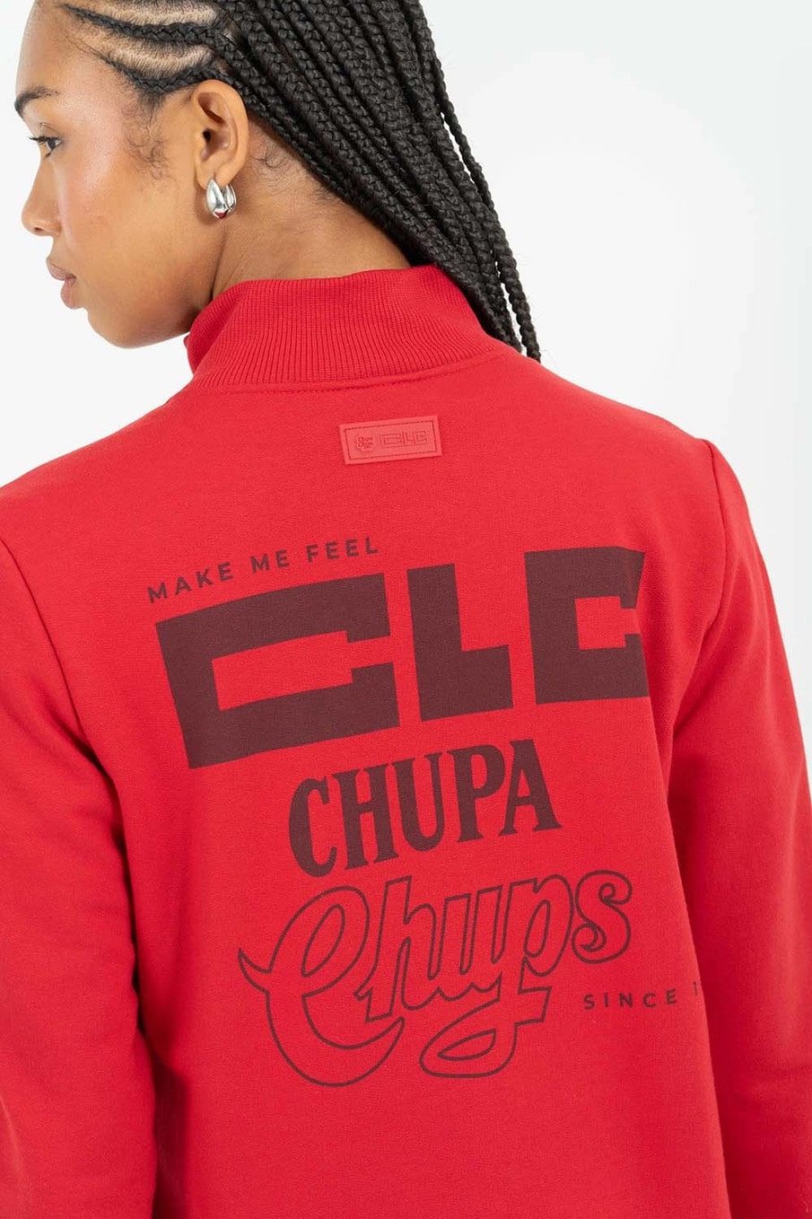 Uma visão aproximada das costas de uma mulher vestindo um moletom vermelho com a marca estampada, incluindo as palavras "MAKE ME FEEL", "CLC" e "Chupa Chups" em letras estilizadas.