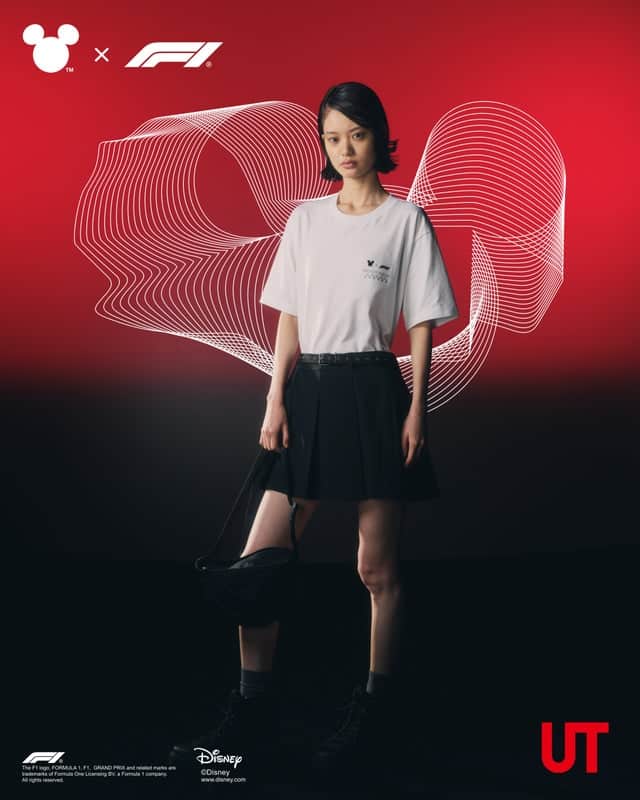 A model wearing a white t-shirt featuring a Mickey Mouse design, paired with a black pleated skirt and boots, stands against a red background with flowing line graphics. The image promotes a collaboration between Disney and Formula 1.