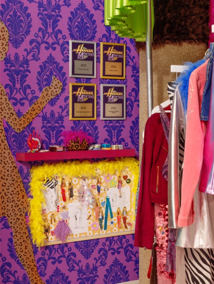 Exposição colorida de esboços de moda e prêmios em uma parede roxa, com uma silhueta de estampa de leopardo e decorações vibrantes.