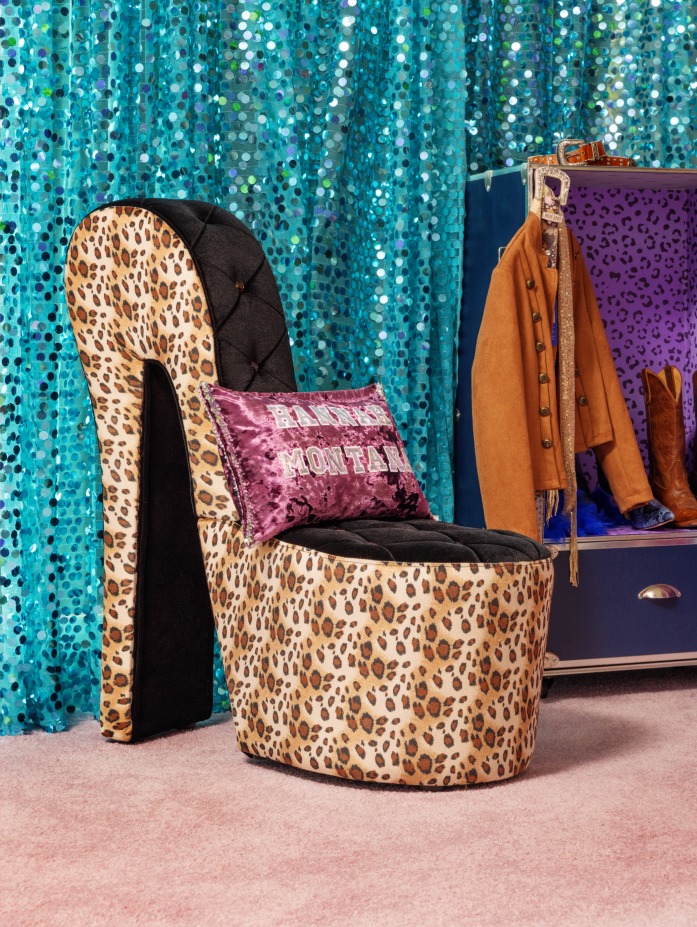Uma elegante cadeira de salto alto com estampa de leopardo e encosto preto acolchoado, acompanhada por uma almofada decorativa com a inscrição "Hannah Montana", em um fundo turquesa brilhante e um tapete rosa suave.