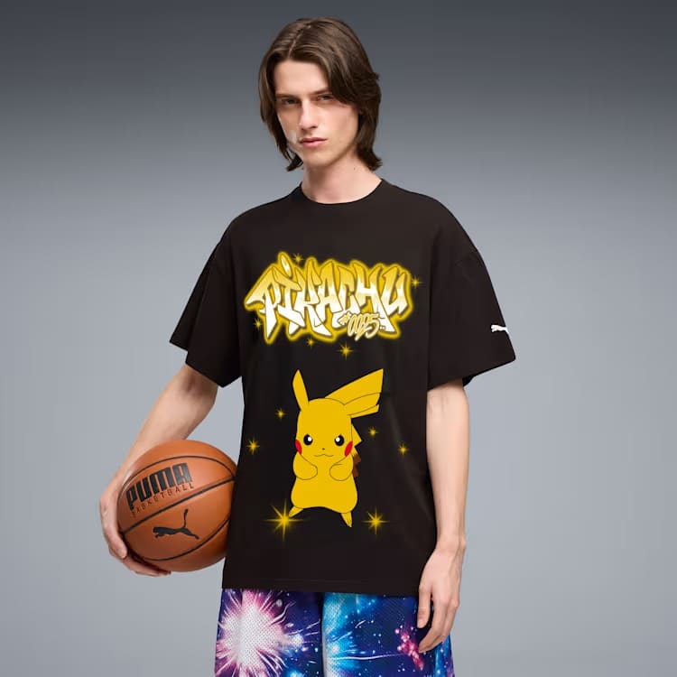 Jovem segurando uma bola de basquete, vestindo uma camiseta preta grande com estampa do Pikachu e texto em estilo grafite, combinada com shorts estampados coloridos.