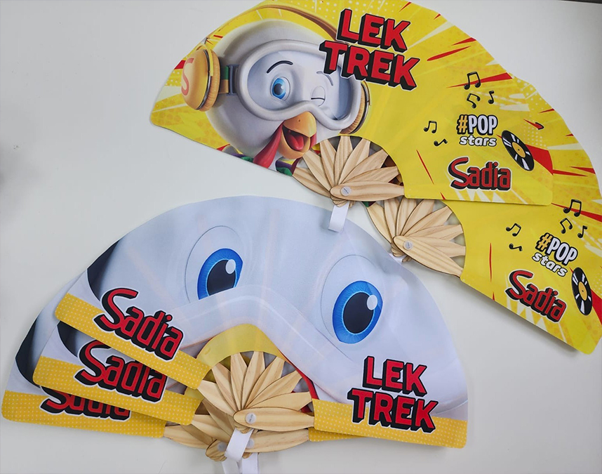Dois leques de papel decorativos com desenhos de personagens de desenhos animados, um apresentando uma galinha alegre e o outro um pássaro estilizado, ambos com a marca 'Sadia' e a frase 'LEK TREK' em um fundo colorido.