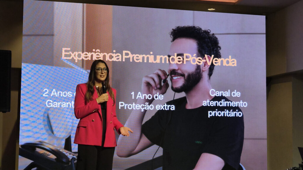 Apresentadora em evento, discutindo experiência premium de pós-venda, enquanto um homem com fones de ouvido aparece ao fundo. Textos destacam benefícios como garantia de 2 anos, proteção extra de 1 ano e atendimento prioritário.