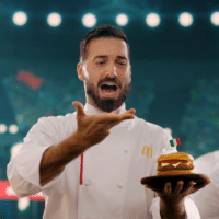 Chef do McDonald’s com sanduíche na mão, em cenário de estádio com clima de Copa do Mundo 2026.