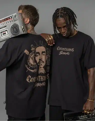 Two men wearing matching black t-shirts with a graphic design on the back featuring a portrait and text. One man holds a vintage boombox.