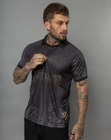 A tattooed man wearing a black short-sleeve polo shirt with graphic designs, posing against a plain background.