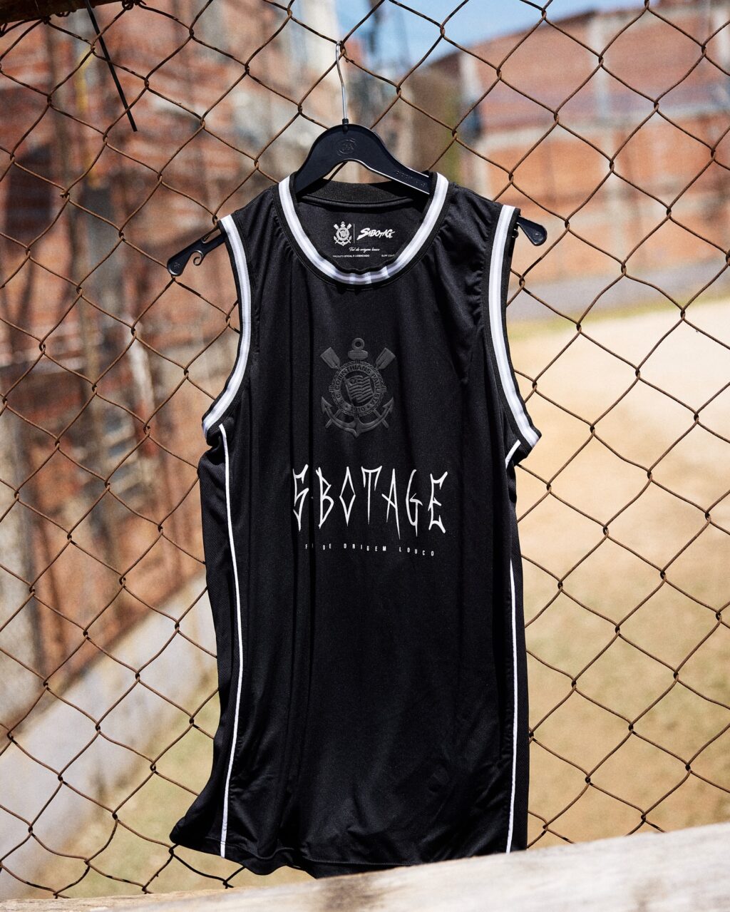 A black basketball jersey hanging on a chain-link fence, featuring the word 'SBOTAGE' in bold, stylized font.