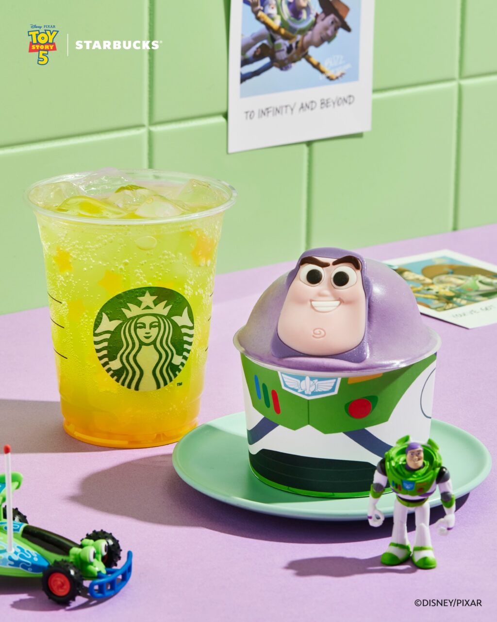 A colorful Starbucks drink and a themed dessert featuring Buzz Lightyear from Toy Story, with a toy figure of Buzz and a playful car toy on a purple surface.