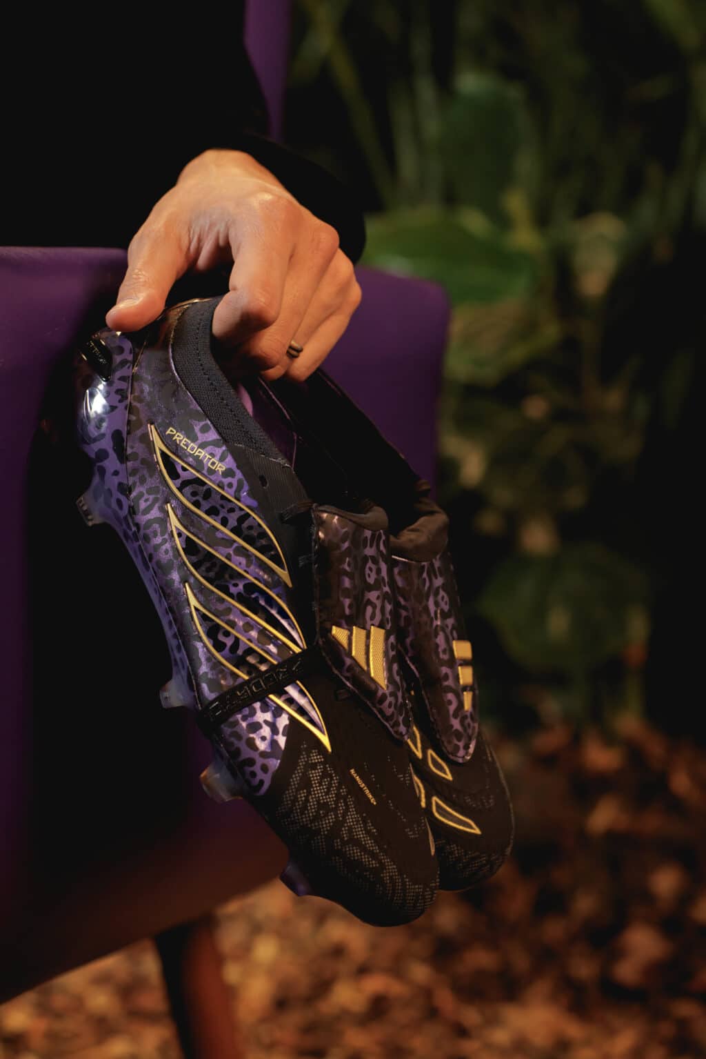 Mão ajustando a chuteira Adidas Predator Kaká Signature preta e roxa com detalhes em dourado