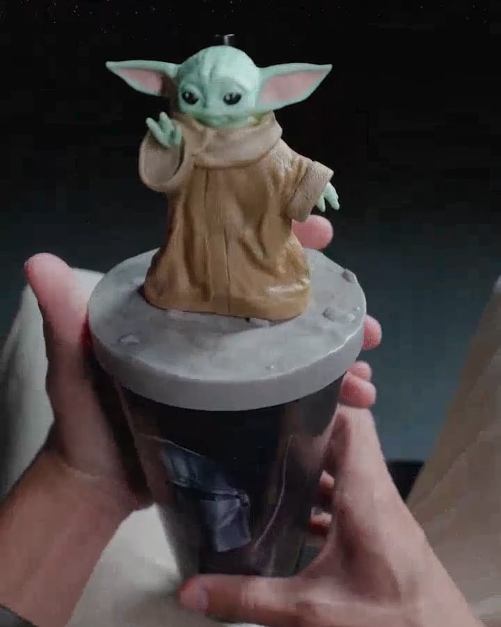 Copo Star Wars com personagem Grogu, segurado por mãos em ambiente escuro, em promoção da Cinemark.