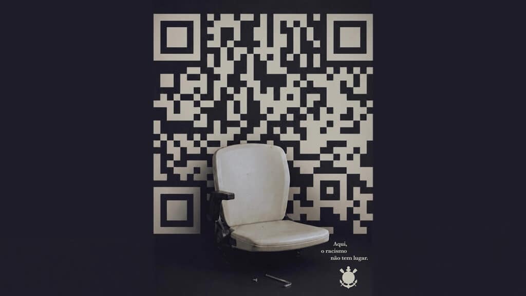 Banco em estádio ao lado de código QR com mensagem de conscientização do Corinthians contra o racismo.