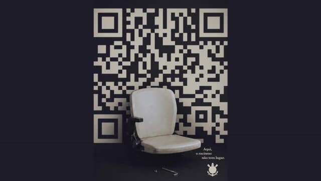 Banco em estádio ao lado de código QR com mensagem de conscientização do Corinthians contra o racismo.