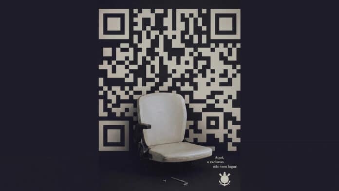 Banco em estádio ao lado de código QR com mensagem de conscientização do Corinthians contra o racismo.