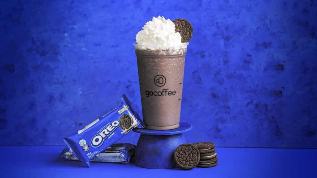 Copo de frapuccino Go Coffee com biscoitos Oreo ao lado, em fundo azul