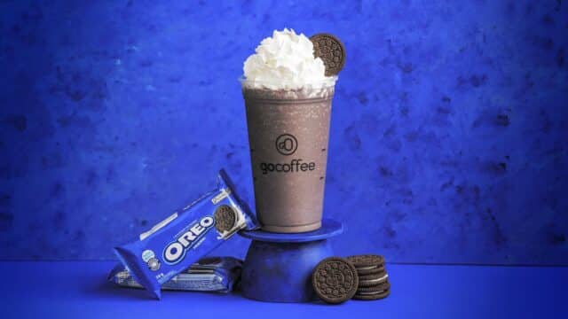 Copo de frapuccino Go Coffee com biscoitos Oreo ao lado, em fundo azul