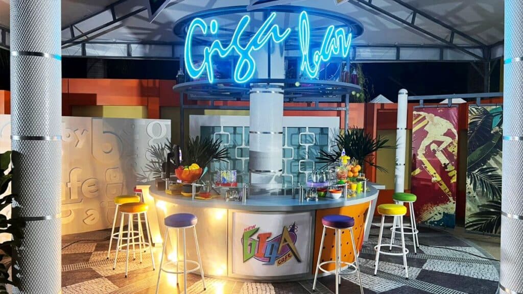 Área do GigaByte Café com balcão decorado, mesas altas e letreiro neon colorido ao fundo, em evento em São Paulo.